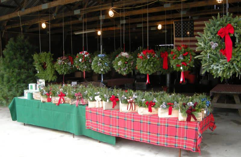 A long table of decorated wreaths with red bows, more wreaths hanging above